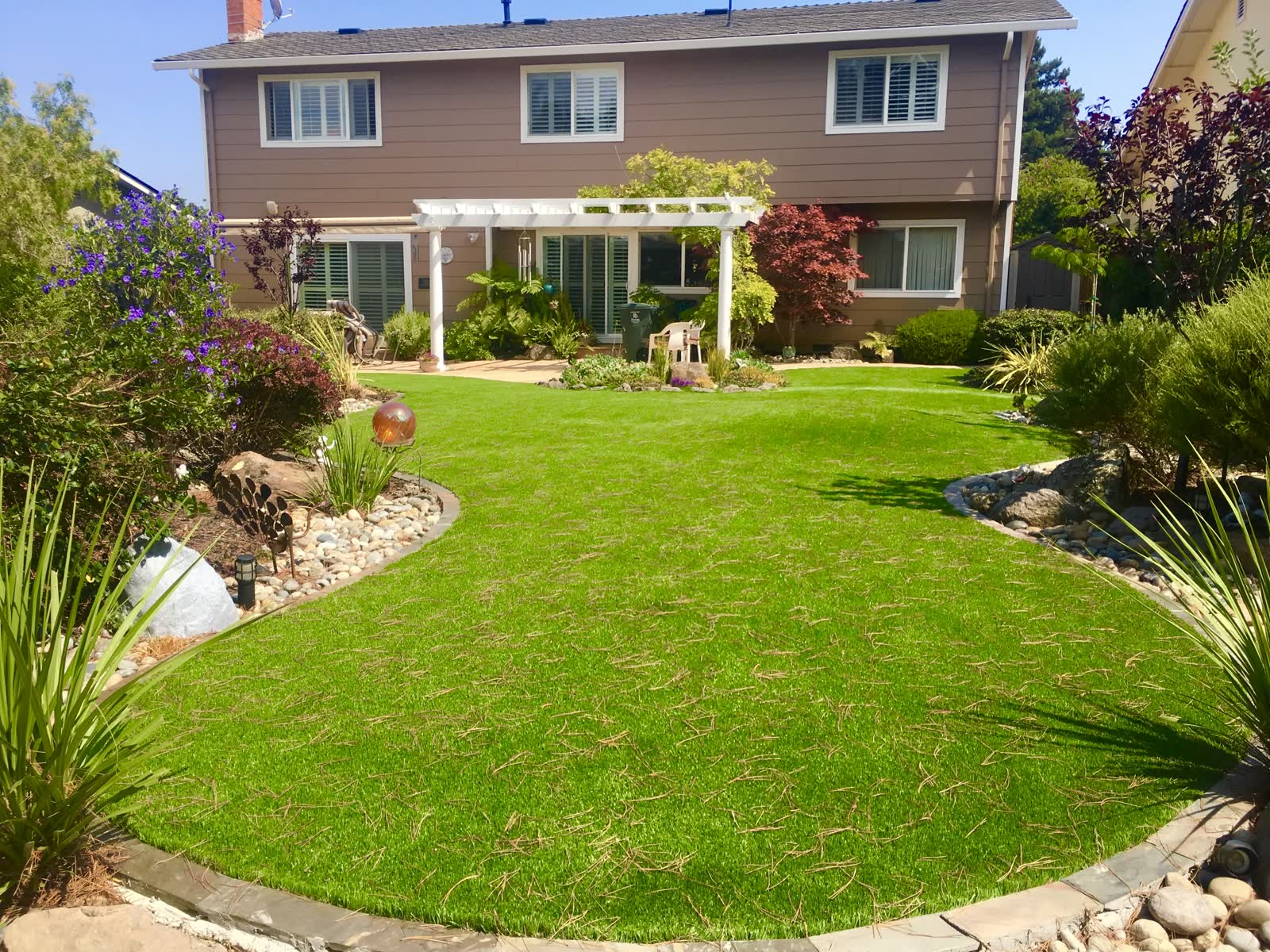Wide backyard with a white pergola, curved turf lawn, rock-edged beds and path lighting