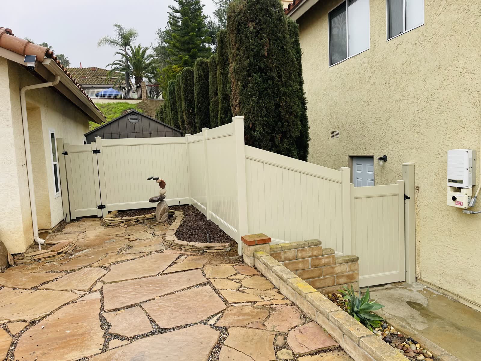 Tan vinyl privacy fence and gate above a flagstone patio with brick steps