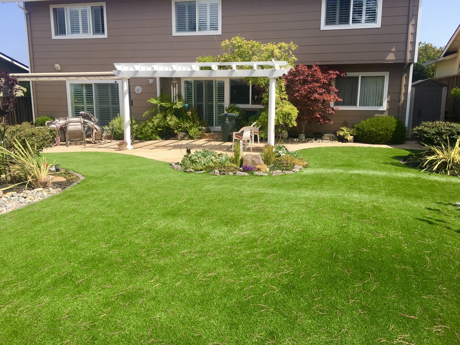 White pergola over a paver patio with turf lawn and rock-edged planting beds